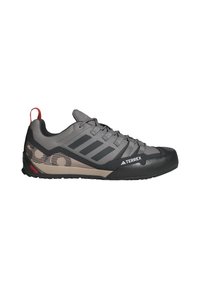 Chaussure de randonnée Adidas Terrex grise et noire avec lacets, embout renforcé, motif latéral beige et languette rouge au talon sur fond blanc.