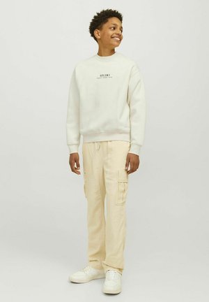 Helles beiges Sweatshirt mit Rundhalsausschnitt und dem Aufdruck "STUDIO." Kombiniert mit hellbeigen Cargo-Hosen mit Seitentaschen und elastischen Bündchen.