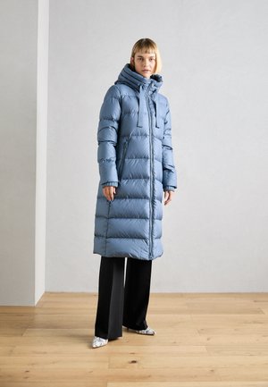 Padded long coat in light blue with a hood, featuring zip closure and two side pockets. Paired with black wide-leg pants and patterned shoes.