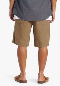 Pantalones cortos caquis con bolsillos laterales tipo cargo, fabricados en tejido ligero. Presentan un corte holgado y un dobladillo que cae por encima de la rodilla.