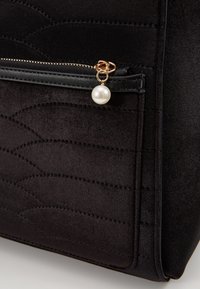 Czarna welurowa torebka z pikowanym texturem, z kieszonką na zamek błyskawiczny oraz perłowym akcentem na uchwycie zamka. Gładkie czarne skórzane wykończenie.