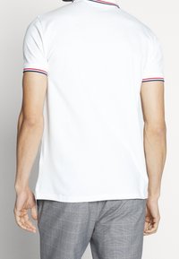 Męska biała koszulka polo z żeberkowym kołnierzykiem z czerwonymi i niebieskimi akcentami. Krótkie rękawy, prosty dół i gładka bawełniana faktura.