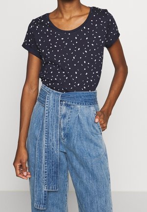 Marineblauw t-shirt met korte mouwen en een wit verspreid stippenpatroon, gecombineerd met lichtblauwe denim broek met hoge taille en een gestrikt riem.