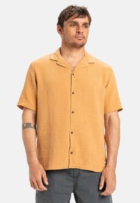 Short-sleeve, button-up shirt in mustard yellow fabric, featuring a textured finish, spread collar, and brown buttons.