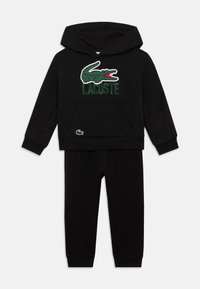 Conjunto de sweatshirt com capuz e calças para crianças negras, com o logo do crocodilo verde da Lacoste e o nome da marca no peito.