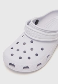 White rubber clog with ventilation holes, a textured outsole, and a flexible strap. Features a raised logo on the strap.
