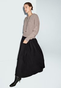 Maglione marrone lavorato a maglia con maniche lunghe, abbinato a una gonna maxi nera e fluida, completato da stivali neri al ginocchio.