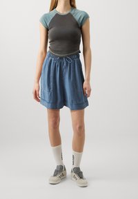 Šedý a tyrkysový krátký rukáv top spárovaný s světle modrými, ke kolenům sahajícími šortkami s elastickým pasem a dvěma předními kapsami.