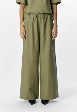 Pantalons ample vert olive fabriqués dans un tissu texturé, dotés d'une taille élastique avec cordon de serrage et de poches latérales.