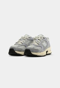 Chaussures de sport en maille grise et en daim avec des accents clairs, bout rond, semelles épaisses et lacets plats. Marquage notable sur le côté.