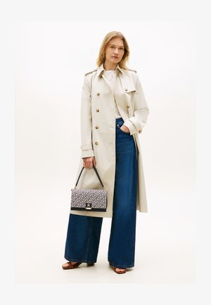 Vrouw draagt beige trenchcoat, wit topje, wijde blauwe jeans, bruine sandalen en houdt een patroonhandtas met zwarte band vast.