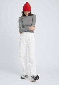 Haut à rayures à manches longues avec un logo rouge, associé à un pantalon blanc taille haute. Le mannequin porte des baskets grises et noires, complétées par un bonnet tricoté rouge.