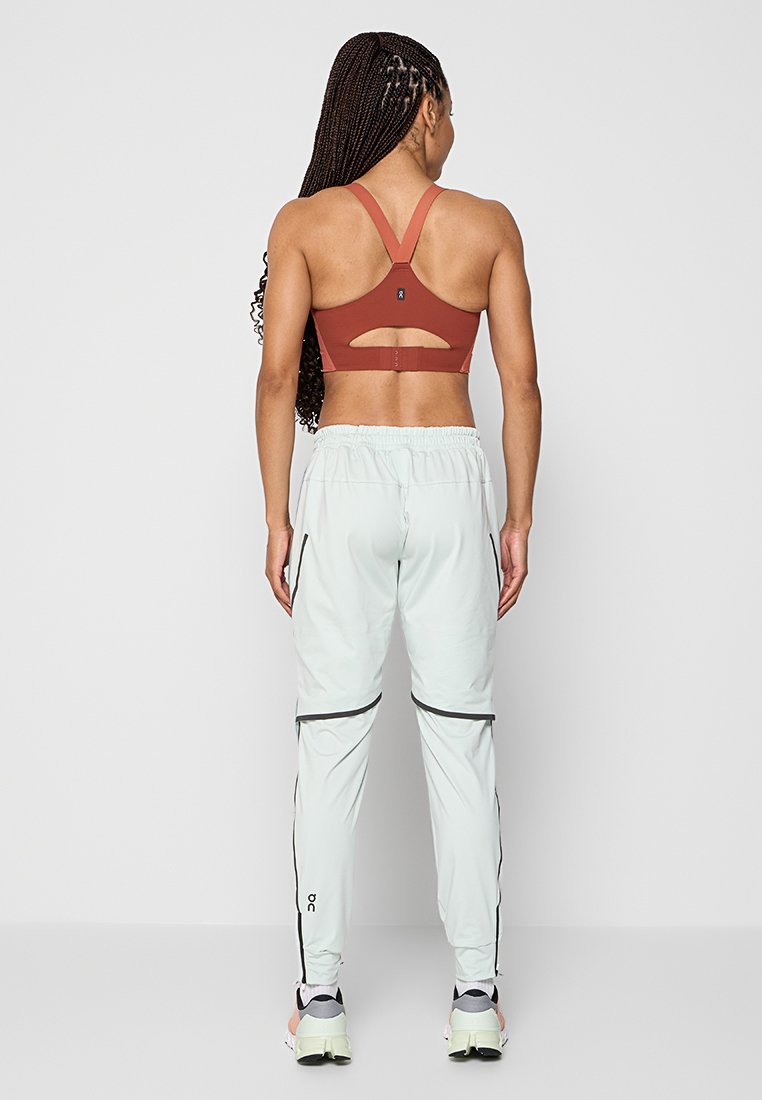 Sport-BH in rostrot mit einem ausgeschnittenen Rücken; kombiniert mit hellen Mint-Jogginghosen mit schwarzen Reißverschlusselementen und einem Kordelzug am Bund.