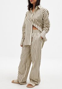 Randig pyjamaset i beige och brunt, med en skjorta med knappar i avslappnad passform och matchande byxor med löst skärning och resårmidja.