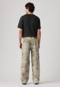 Ανοιχτό γκρι τζιν με φαρδιά μπατζάκια και χοντρή υφή, με δύο πίσω τσέπες· συνδυασμένα με κοντομάνικη μαύρη μπλούζα.