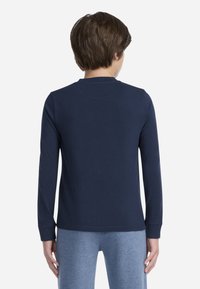 Chemise à manches longues bleu marine avec un col rond, fabriquée en coton doux, présentant un design simple et une coupe régulière, portée avec un pantalon gris.