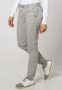 Světle šedé bavlněné kalhoty s úzkým střihem, které mají postranní kapsy a jemné detaily šití. V kombinaci s bílými botami a šedými ponožkami.