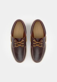 Brune skinnsko med glatt overflate, rund tå og beige såle. Har gullhull og brune lisser. Innvendig er de tannfargede.
