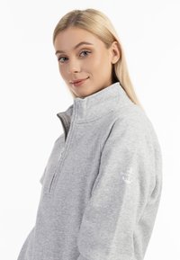 Lys grå fleece pullover med kvart-lynlås, blød tekstur og broderet ankerdetalje på venstre ærme.