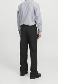 Uomo visto di spalle che indossa una camicia grigia chiaro con bottoni e pantaloni neri. Tessuto non testurizzato, vestibilità standard, con due tasche posteriori e bottoni neri.