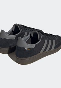 Svarta och mörkgrå Adidas-sneakers med Cordura-tygskylt, mocka häl, tre randiga detaljer på sidorna och strukturerade mörka gummisulor.