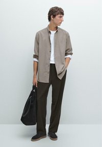 Light brown button-up shirt over a white t-shirt, paired with dark green pants and a black tote bag. Brown shoes complete the look.