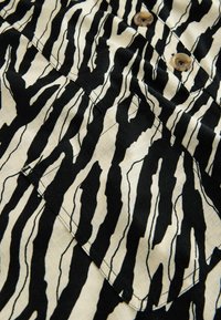 Nahaufnahme von schwarz-weiß zebragestreiftem Stoff mit einer Tasche und zwei braunen Knöpfen an einem Kleidungsstück.