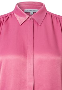 Rosa Bluse mit klassischem Kragen, glatter Textur und Knopfverschluss, mit gefälteltem Detail an den Schultern. Größenetikett sichtbar.