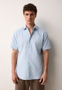 Camicia azzurro chiaro a maniche corte con sottili righe bianche, design con colletto e chiusura frontale con bottoni; trama liscia, vestibilità casual.