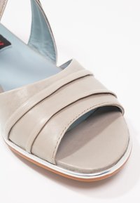 Sandale en cuir gris clair avec trois lanières horizontales, design à bout ouvert, doublure bleue et semelle en caoutchouc avec un fin accent blanc.