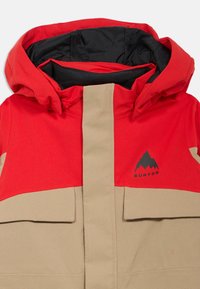 Rode en beige winterjas met een hoge kraag, zwarte voering en twee voorkonten; heeft een logo van een berg aan de linkerkant.