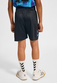 Svarta shorts med elastisk midja, prydda med ett blått chevronmönster på den nedre sidan. Vita strumpor med svart chevronmönster och sneakers.