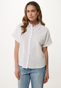 Biała lniana koszula z guzikami z przodu, krótkimi rękawami, wywiniętym kołnierzykiem i luźnym krojem. Nosi się z jasnoniebieskimi dżinsami.