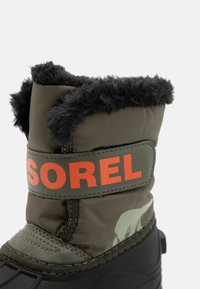 Žalios vandeniui atsparios žiemos bootai, su puria juoda kailių apdaila viršuje ir oranžiniu "SOREL" logotipu. Tekstūruota guminė padanga geresniam sukibimui.