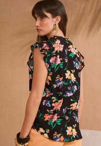 Blouse noire à motifs floraux avec des manches courtes à volants, des motifs floraux colorés en rose, orange et bleu, et une coupe ample.