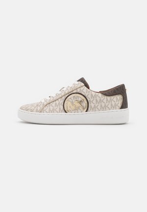 Beige lav-top sneaker med hvid sål, brun kant, snørelukning foran og et gennemgående "MK" logo mønster med en rund Michael Kors emblem på siden.