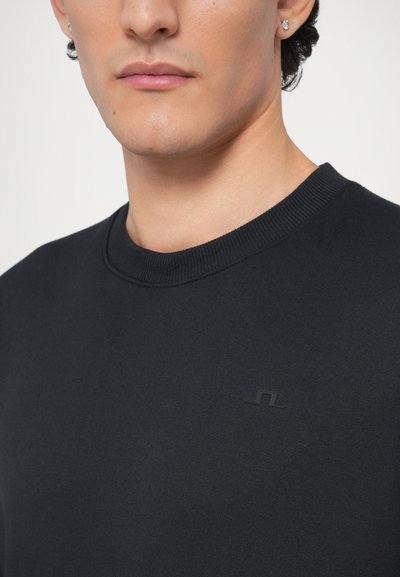 Μαύρο φούτερ με στρογγυλή λαιμόκοψη, ριμπ ύφανση στη λαιμόκοψη, απαλό ύφασμα και διακριτικό ανάγλυφο λογότυπο στην αριστερή πλευρά.