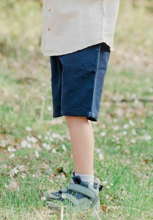 Marineblå shorts lavet af letvægtsmateriale, med et enkelt design og synlige stikninger. Fodtøj: grå og grønne velcro-sko.