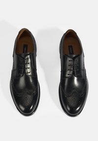 Zwarte leren brogue schoenen met patroon, ronde neus, vetersluiting en een gladde textuur. Bruine leren binnenzool zichtbaar.