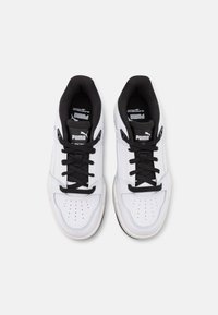 Bílé kožené tenisky s černými akcenty a tkaničkami, s perforovaným designem špičky a polstrovaným černým interiérem. PUMA branding na jazyku.
