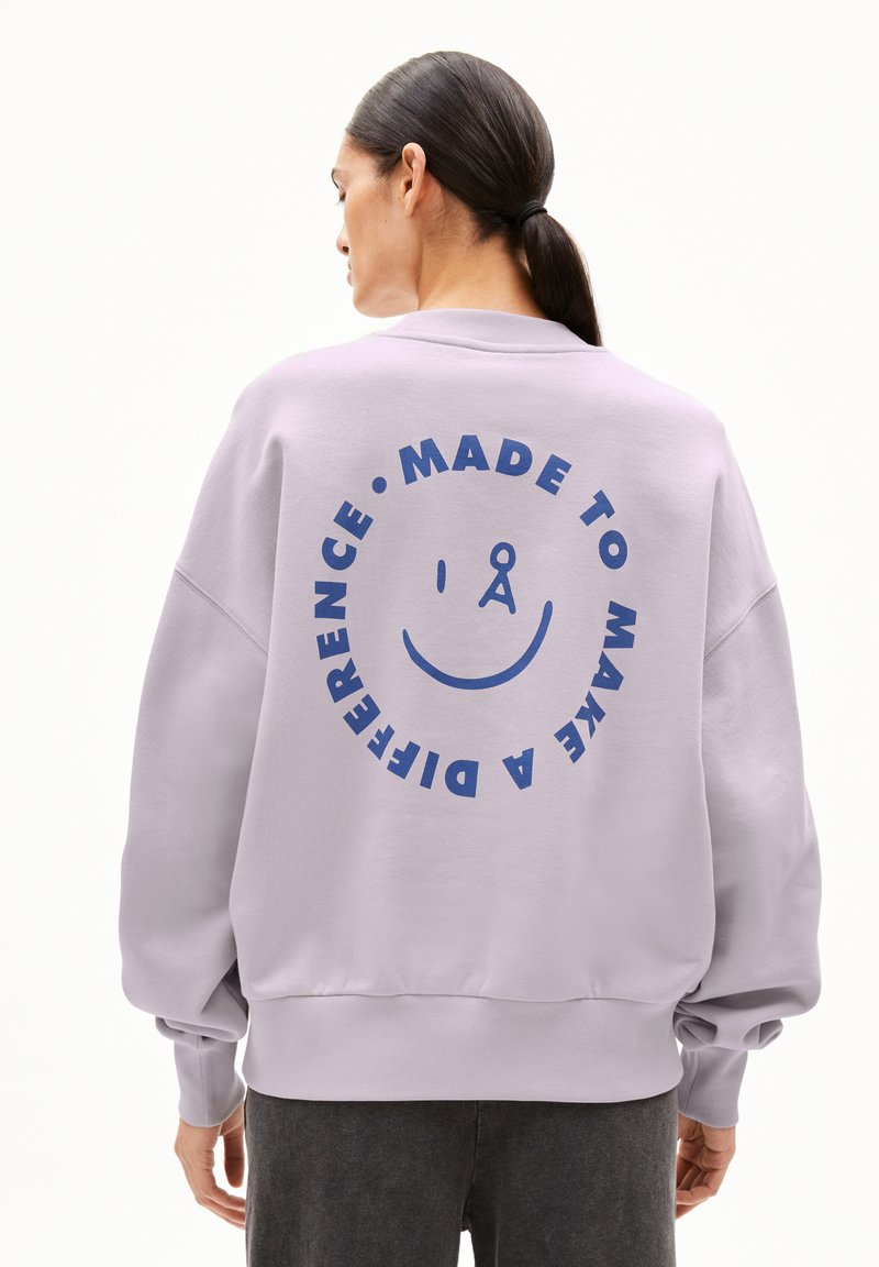 Lila sweatshirt met een boxy ontwerp, voorzien van een grote blauwe grafische print op de achterkant met de tekst "MADE TO MAKE A DIFFERENCE" en een glimlachend gezicht.