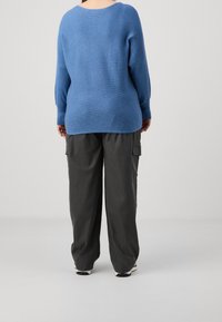 Maglione blu a coste con scollo ampio e maniche lunghe, abbinato a pantaloni cargo grigi con tasche e vestibilità rilassata.