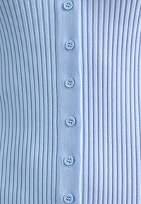 Světle modrá žebrovaná tkanina se svislou řadou sedmi odpovídajících čtyřdírkových knoflíků uprostřed.