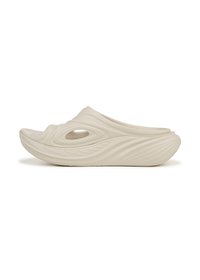 Cream-colored slip-on shoes with a fluid design, featuring a textured exterior, open toe, and circular cutouts for ventilation.