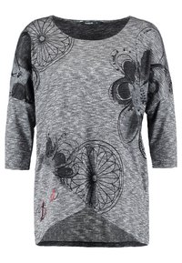 Grauer Strickoberteil mit drei Viertel-Ärmeln. Verfügt über schwarze Blumenmuster und kreisförmige Designs. Begleitet von roten Stickdetails am Saum.