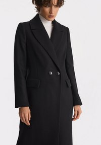 Czarny płaszcz z wełny z domieszką, z podwójnym zapięciem, ostrymi klapami, dwoma przednimi kieszeniami i fakturowanym materiałem.