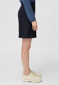 Jupe noire longueur genoux en tissu lisse, dotée de poches latérales et d'une taille simple. Associée à des baskets beige clair.