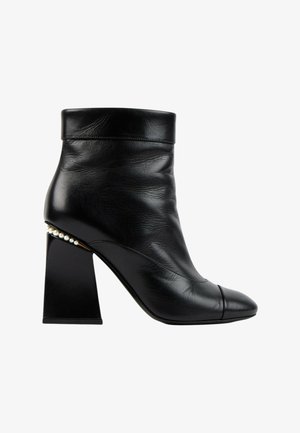 Bottine en cuir noir avec talon bloc et perles décoratives le long du bord du talon, avec un bout arrondi et un revers plié.