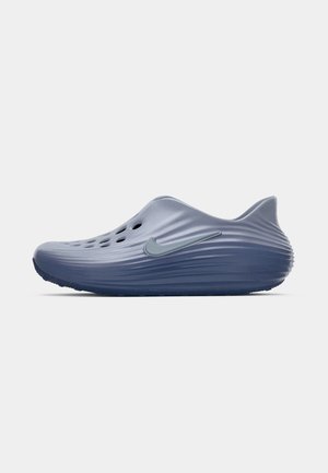 Zila Nike slip-on apava ar ventilācijas caurumiem, teksturētām rieviņām un izteiktu sānu Swoosh logotipu.