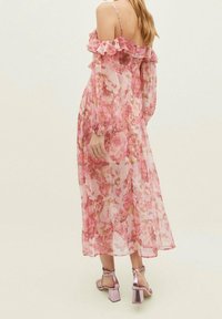 Un vestido largo floral rosa en tejido transparente con mangas de volantes sin hombros y mangas largas en estilo globo. Combinado con sandalias de tacón bloque rosa.